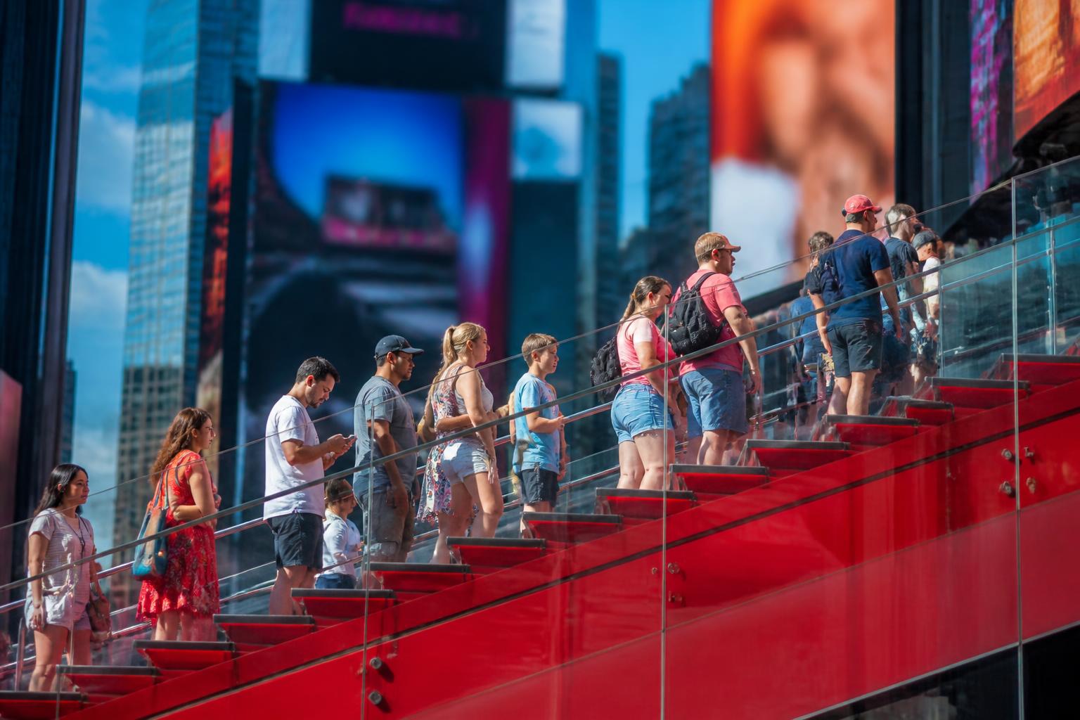 Fila de gente al lado del cubículo rojo de TKTS en Times Square con la pantalla digital mostrando shows disponibles